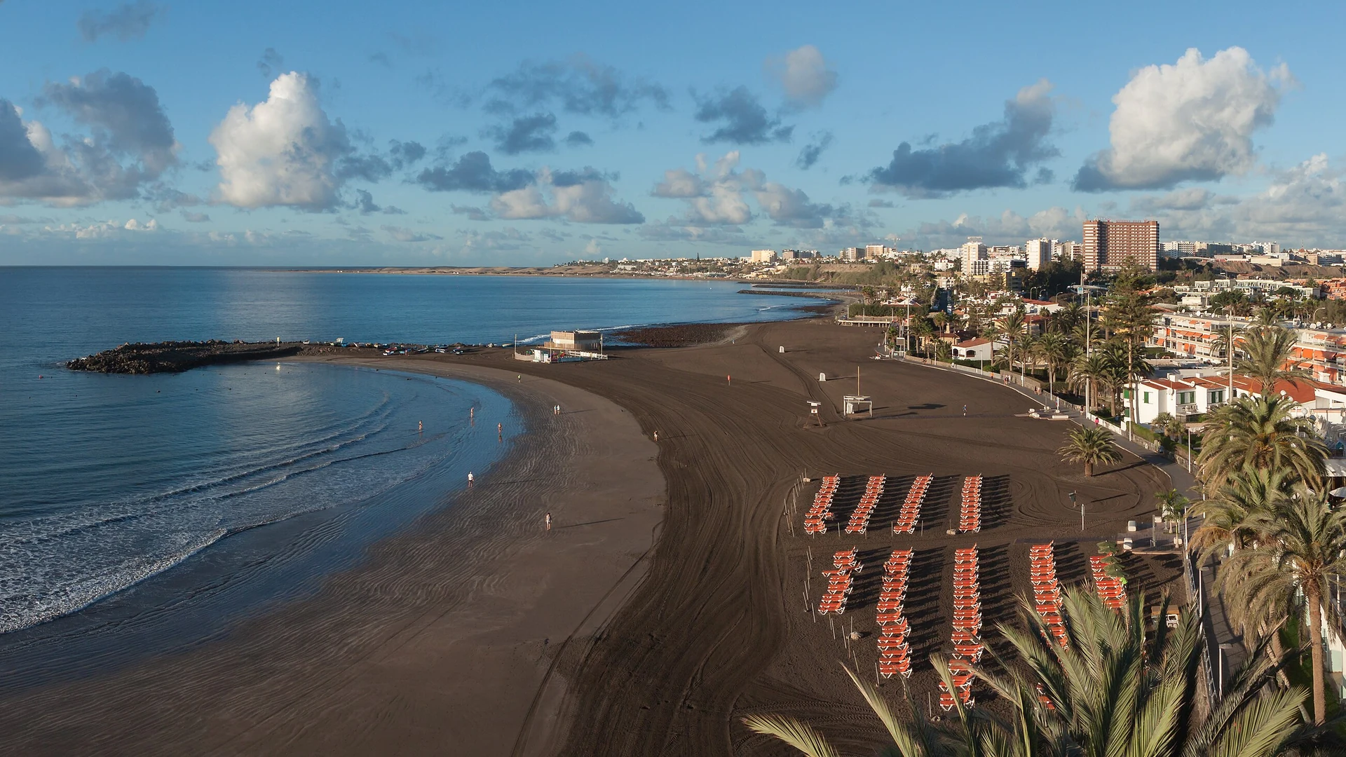 The dark-sand beach at San Agustín on Gran Canaria's south coast, with resort hotels and sunbeds along the promenade
