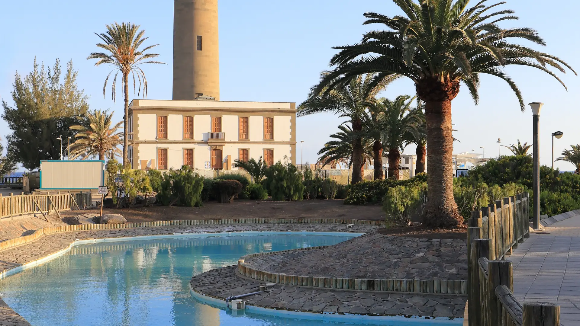 Palm trees and a shallow lagoon pool on the seafront promenade below the Faro de Maspalomas lighthouse, southern Gran Canaria