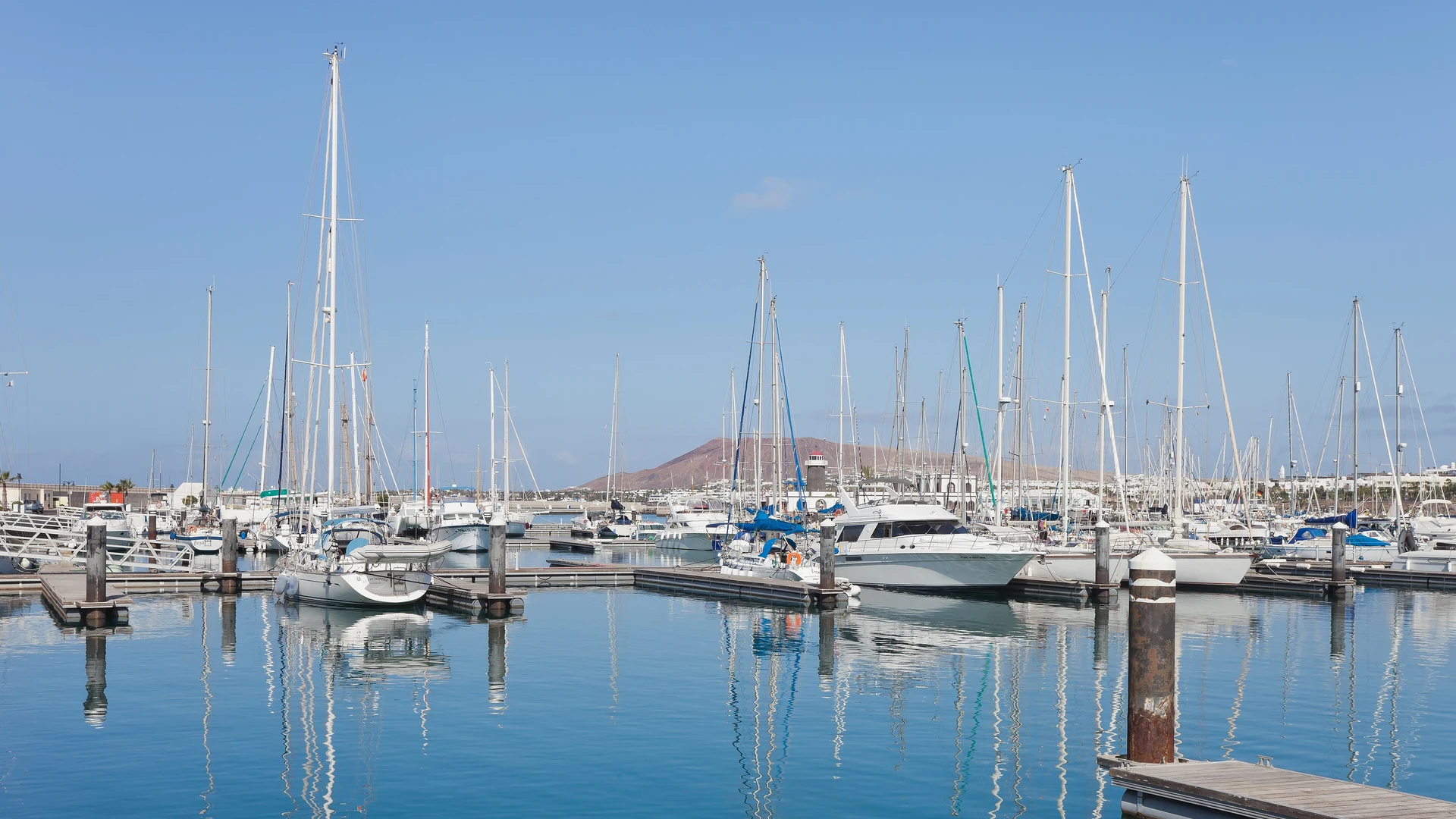 Sailing yachts moored at Marina Rubicón in Playa Blanca, Lanzarote, under a clear blue sky with volcanic hills in the distance