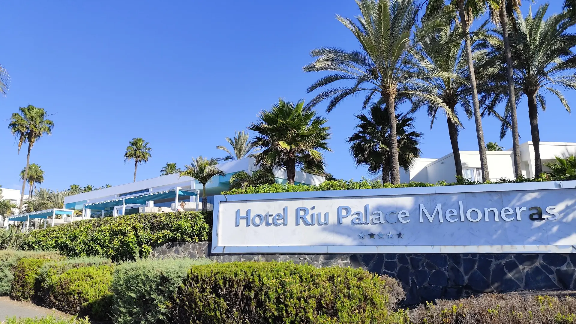 The entrance sign of Hotel Riu Palace Meloneras among palm trees on the Meloneras seafront, Maspalomas, Gran Canaria