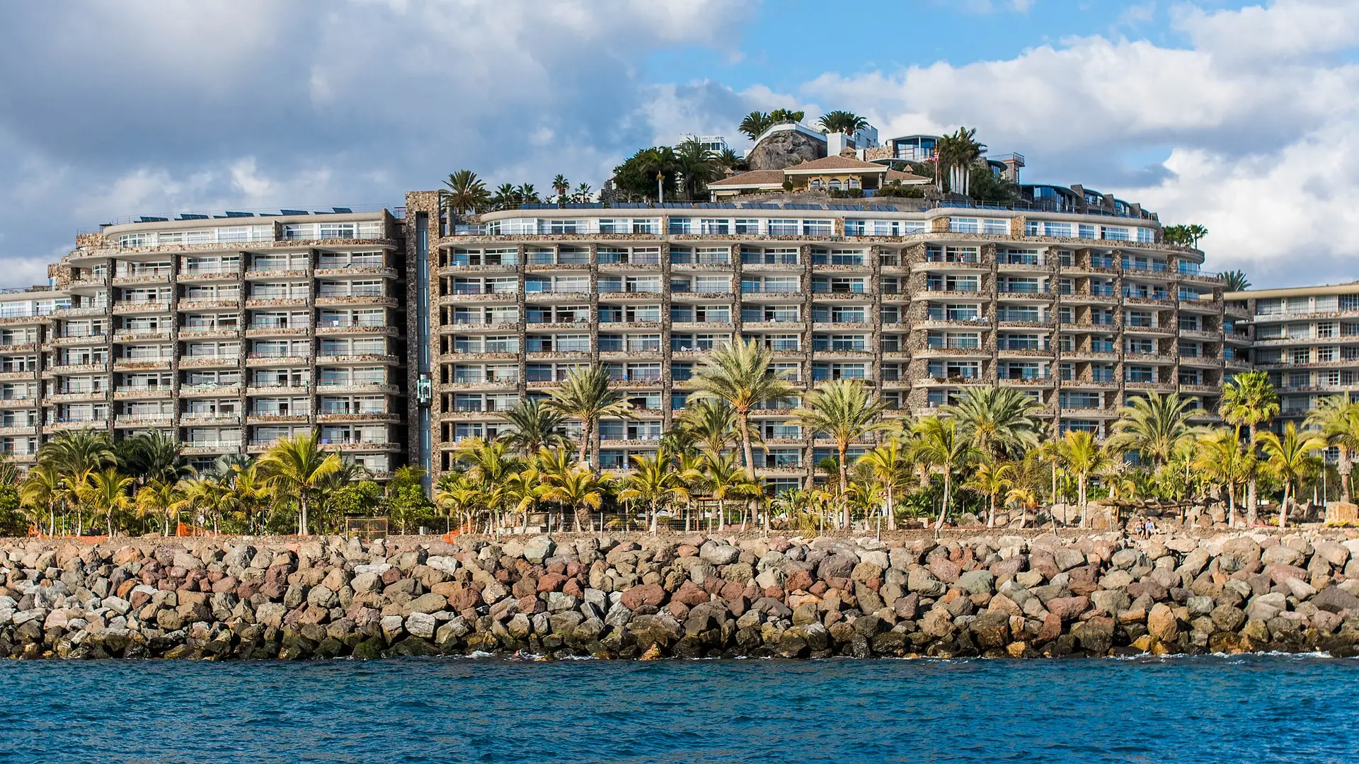 Palm-lined apartment blocks behind the sea wall near Puerto Rico, seen from a boat off Gran Canaria's south-west coast