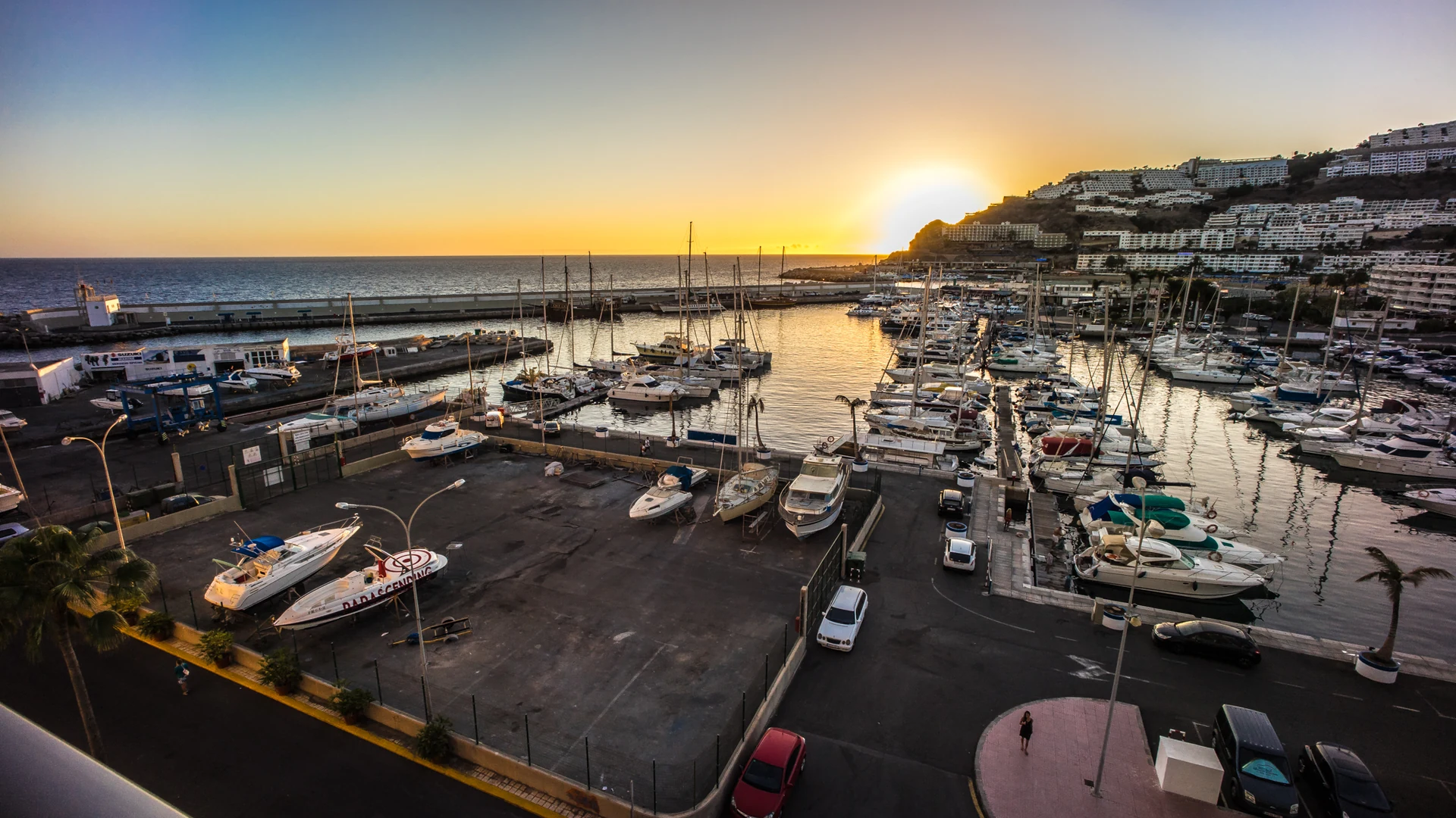 Sunset over the marina at Puerto Rico in south-west Gran Canaria, with boats moored below the cliffs