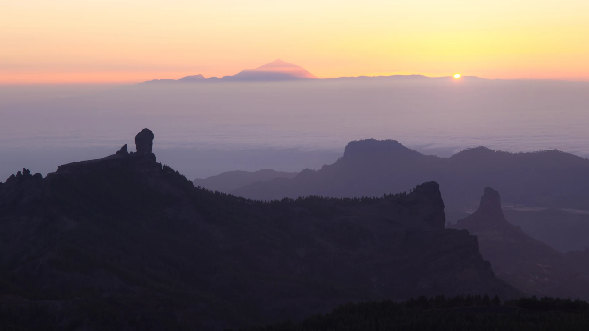 Sunset from Pico de las Nieves over a sea of cloud, with Roque Nublo and Roque Bentayga in silhouette and Mount Teide on the horizon