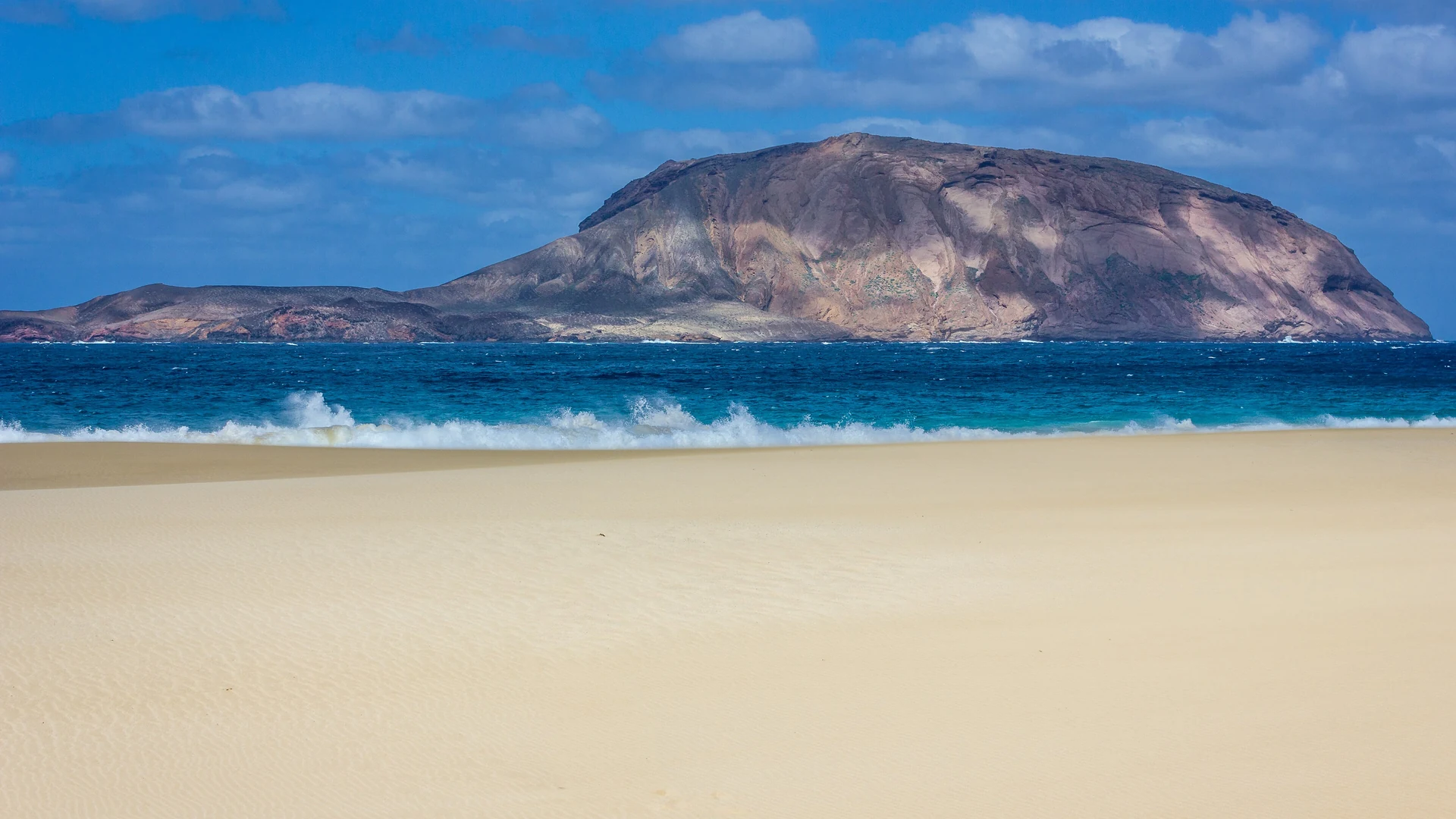 The islet of Montaña Clara seen across the pale sand and surf of Playa de las Conchas on La Graciosa
