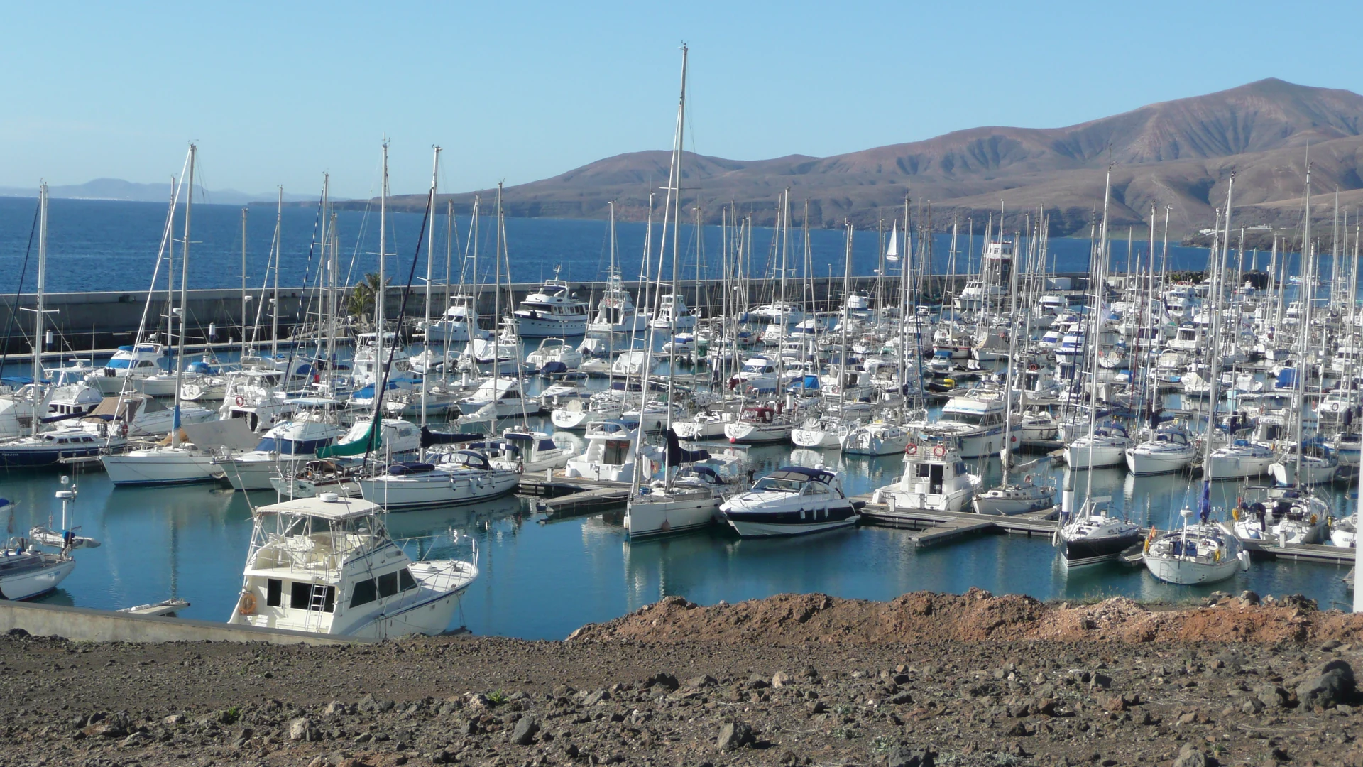Yachts moored in the marina at Puerto Calero, Lanzarote, with brown volcanic mountains behind under a clear blue sky