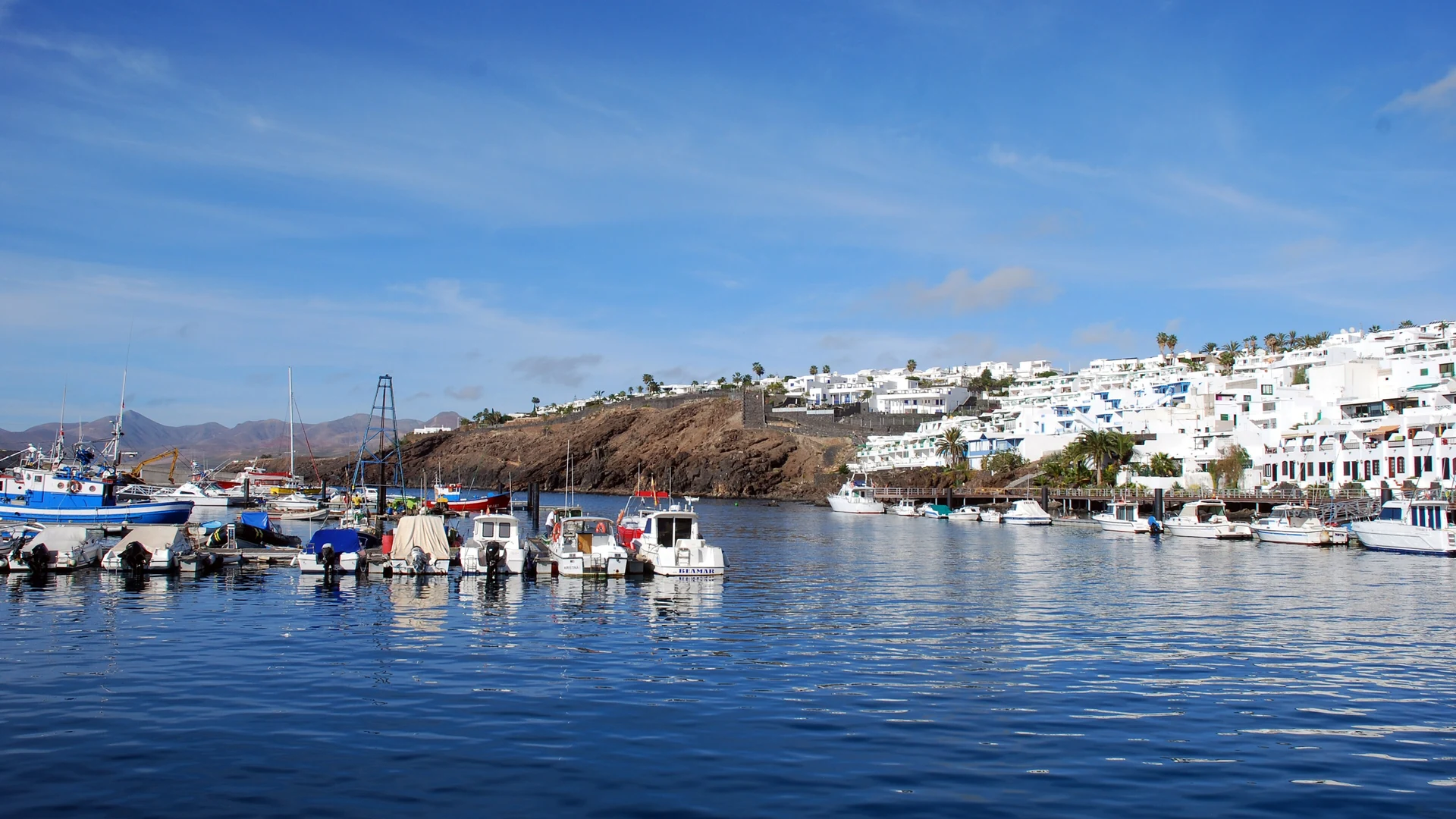 Boats moored in the harbour of Puerto del Carmen, Lanzarote, below the white houses of the old town