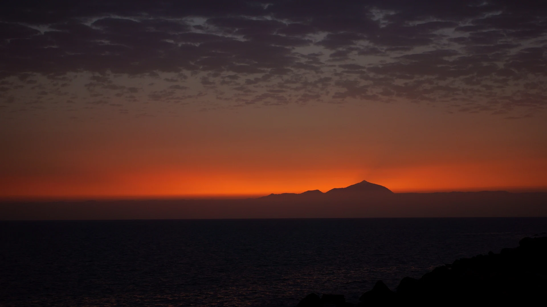 Mount Teide on Tenerife in silhouette against an orange sunset, seen across the sea from Puerto de Mogán on Gran Canaria